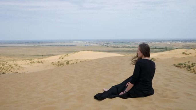 穿着黑色长裙的女人坐在沙漠中的沙丘上