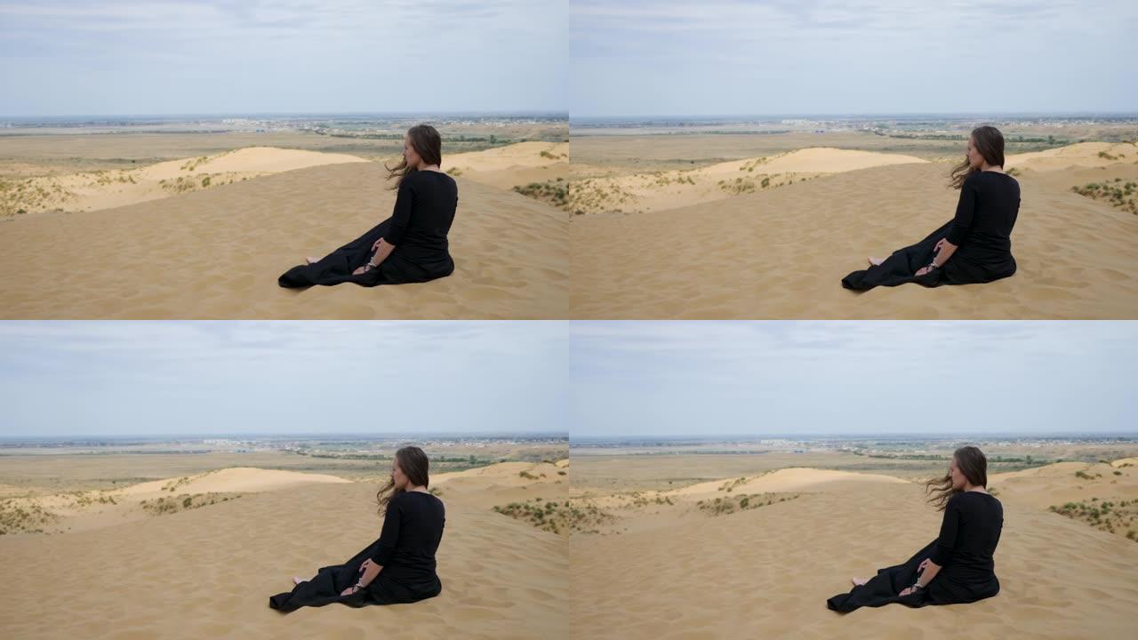 穿着黑色长裙的女人坐在沙漠中的沙丘上