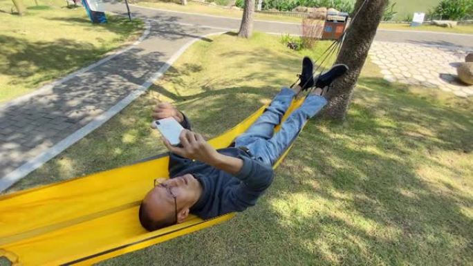 一名亚洲人在树林里的吊床上使用手机的高角度视图