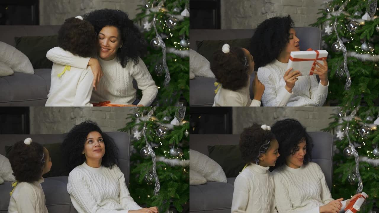 一个非洲裔美国小女孩的肖像给她的母亲带来了惊喜。母女俩坐在沙发旁边，装饰圣诞树。家庭之夜快乐。特写。