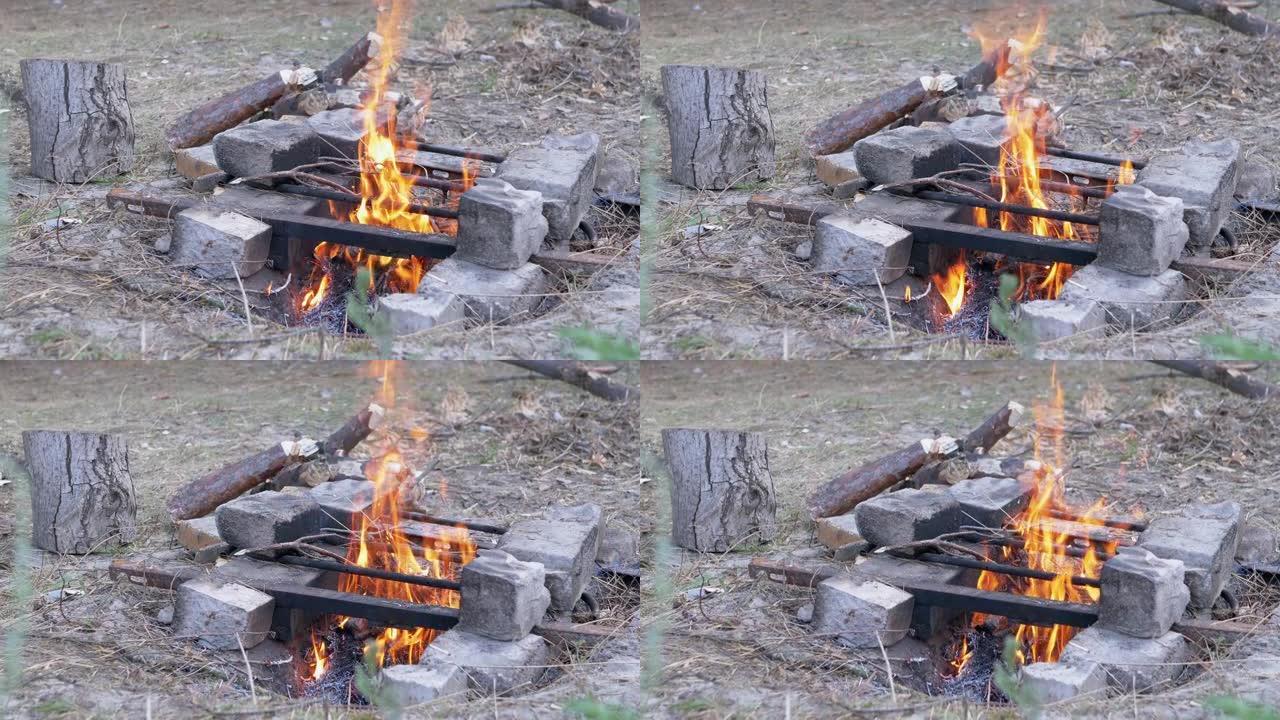 在森林里石头上的金属炉排下的壁炉里燃烧篝火