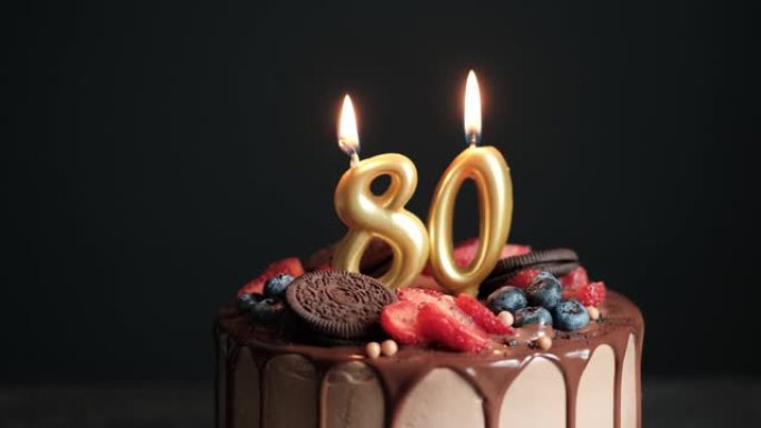黑色背景上的巧克力生日蛋糕，有八十根金色蜡烛。80周年生日蛋糕。慢动作