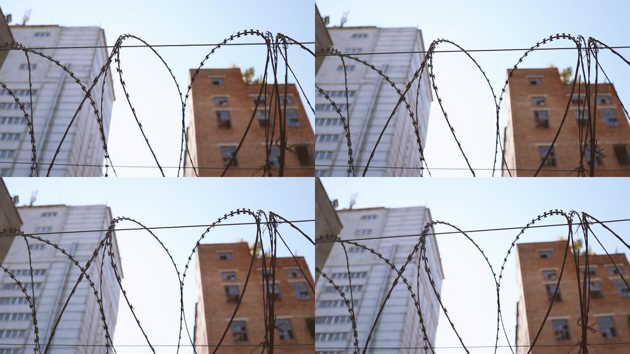 高高的混凝土围栏，铁丝网映衬着蓝天背景。窗户破碎的废弃砖砌建筑