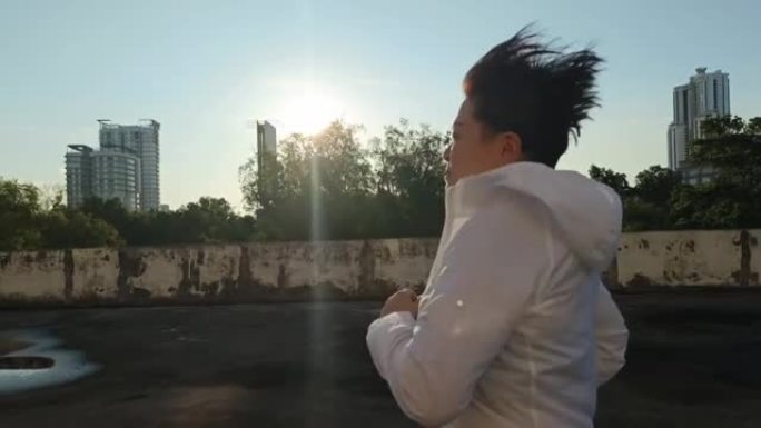 侧视图亚洲中国中年妇女，穿着运动运动服，早上在屋顶停车场跑步