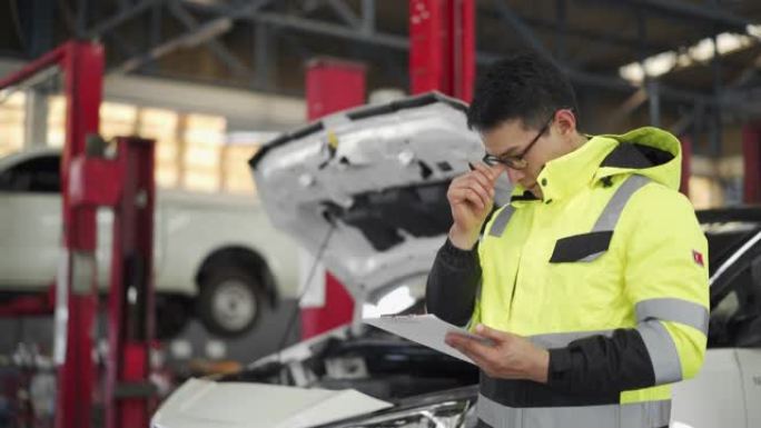 4K男机械师在汽车修理店检查汽车并编写清单