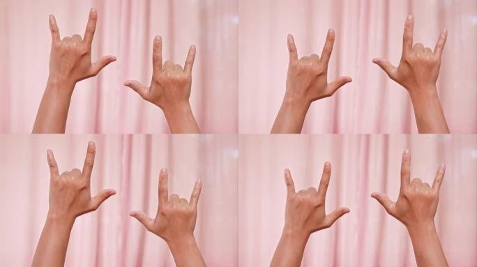 双手在粉红色背景上制作我爱你的符号。女性双手用手语说 “我爱你”。情人节。