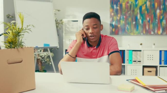 客户顾问坐在笔记本电脑屏幕前的公司办公桌上，在智能手机上交谈，接听呼叫者，将数据输入系统，中断呼叫，