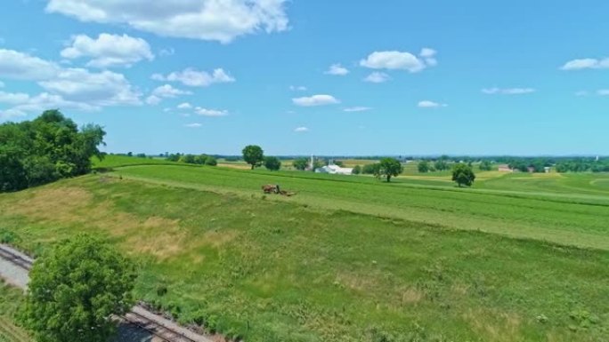 一位阿米什人农民的鸟瞰图，三匹马在收割庄稼时看着一条铁路轨道