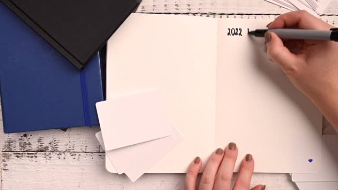 年轻女子在白色背景的笔记本上写2022的计划，用于纸张设计。平躺在木制工作场所上。白色背景。
