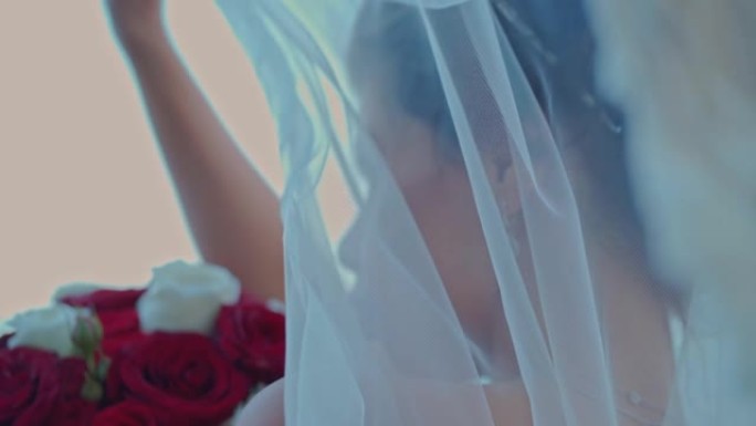 婚礼当天，一位美丽的新娘带着一束玫瑰站在海边的背景下看着相机