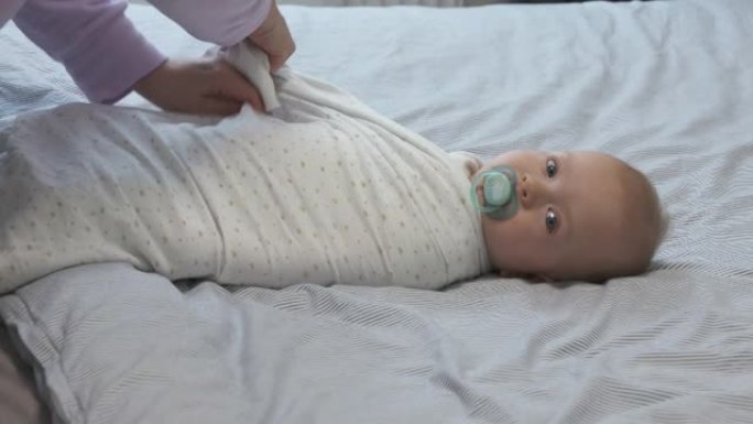 母亲在睡前襁褓婴儿，7个月大的婴儿裹在床上，襁褓有助于防止婴儿挥动胳膊和腿。