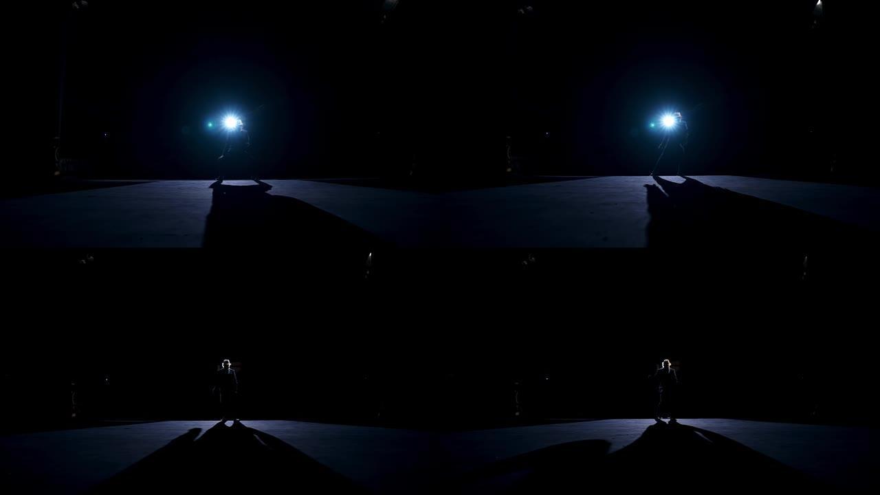 运动中的舞者的剪影。表演者在黑暗背景下的聚光灯下在舞台上跳舞。在剧院表演的人。