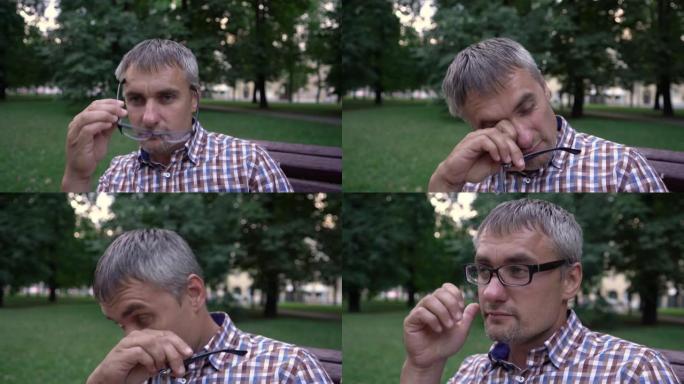男人脱下视力眼镜，在公园里疲倦地擦眼睛