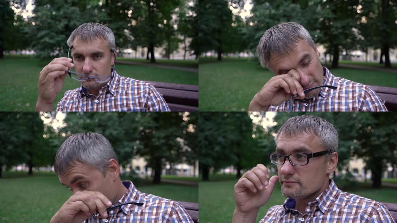 男人脱下视力眼镜，在公园里疲倦地擦眼睛