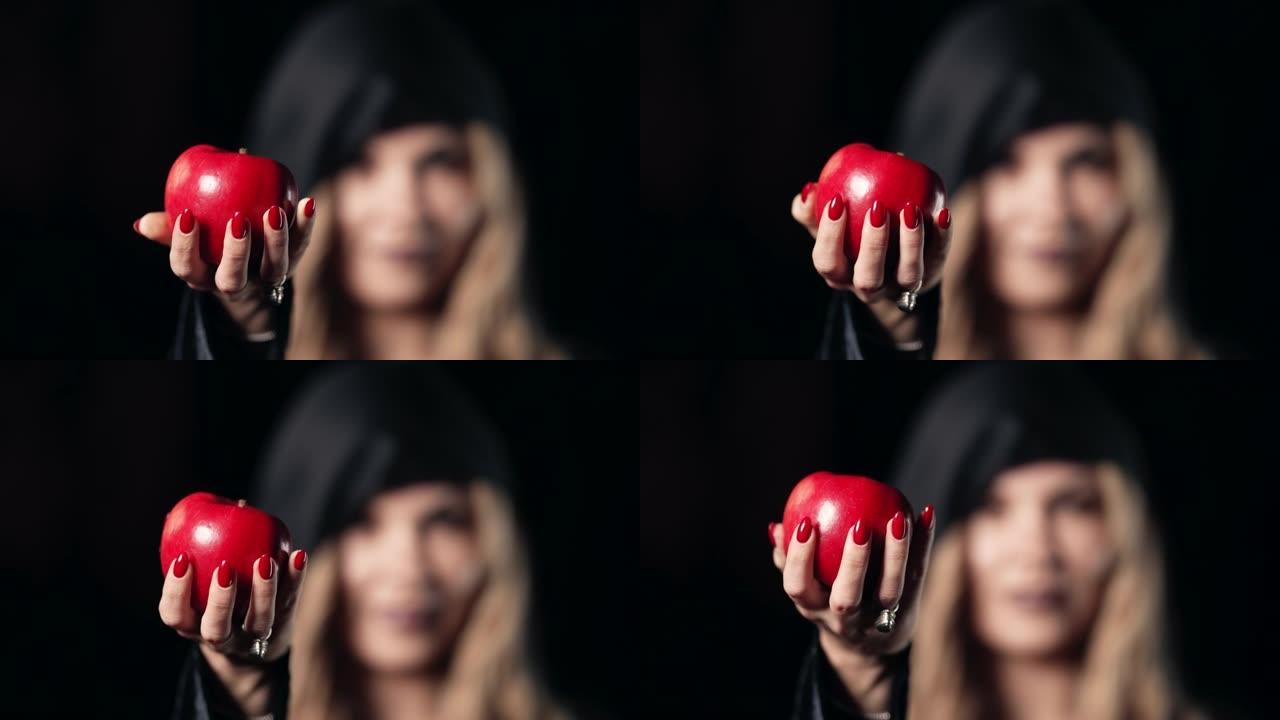 女人作为女巫，带着邪恶的笑容，在黑色中发出红苹果作为诱惑，毒药的象征。童话白雪概念，万圣节，角色扮演