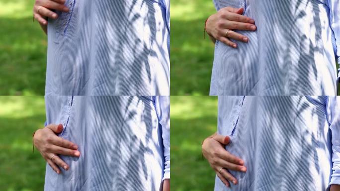 一个拿着结婚戒指的女人的手正通过衬衫抚摸着她怀孕的肚子