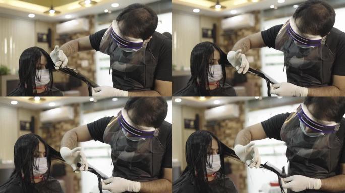 剪掉女性客户头发时戴着口罩和盾牌的男性理发师