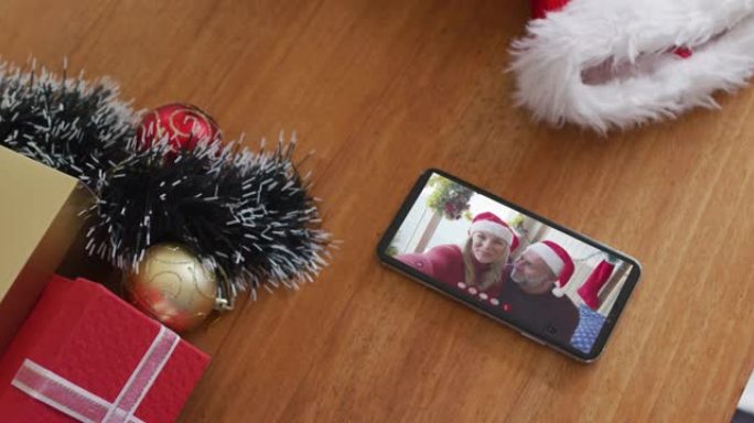 微笑的高加索父亲和女儿戴着圣诞老人的帽子在智能手机上的圣诞节视频通话中