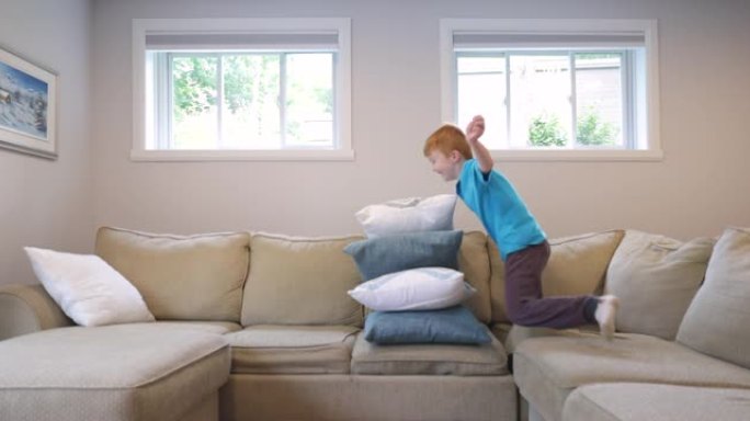 可爱的红发男孩跳过客厅沙发上的垫子