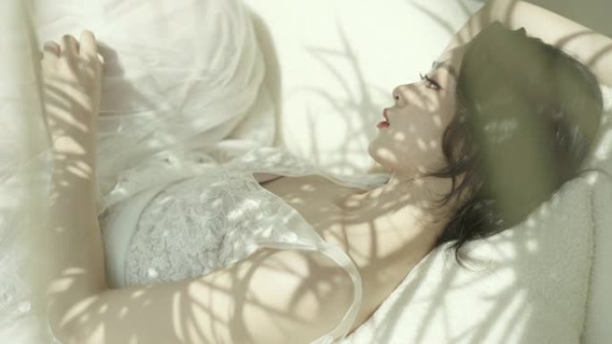 一位穿着白色婚纱的亚洲美女，躺在沙发上，阳光透过树叶照在她身上，慢动作拍摄，中国新娘。