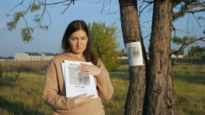 有传单的女人站在靠近失踪狗的海报报道，照片被卡在树干上
