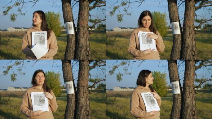 有传单的女人站在靠近失踪狗的海报报道，照片被卡在树干上