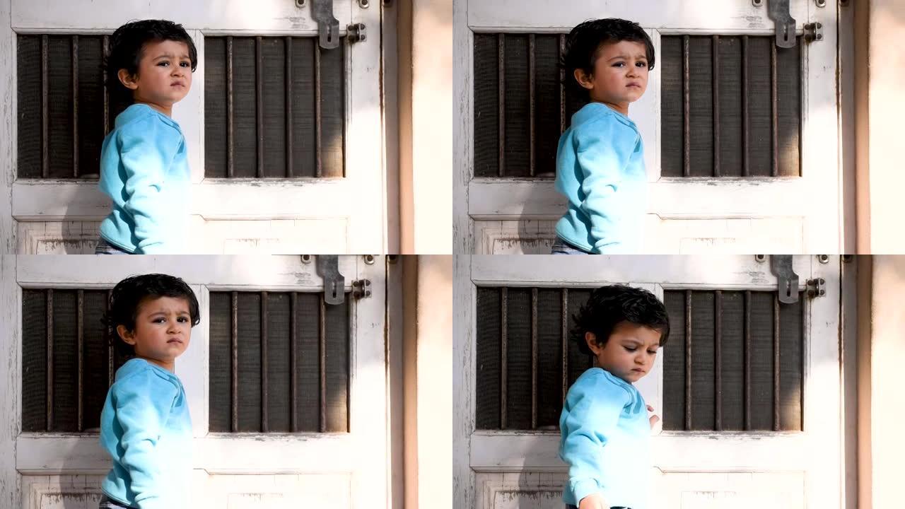 悲伤的印度小孩站在家门口的肖像。顽固的孩子对父母生气