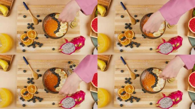 女人用手将种子撒在水果粥的特写镜头上，用浆果和柑橘制成的橙色冰沙碗的俯视图。健康早餐。不含糖的甜食