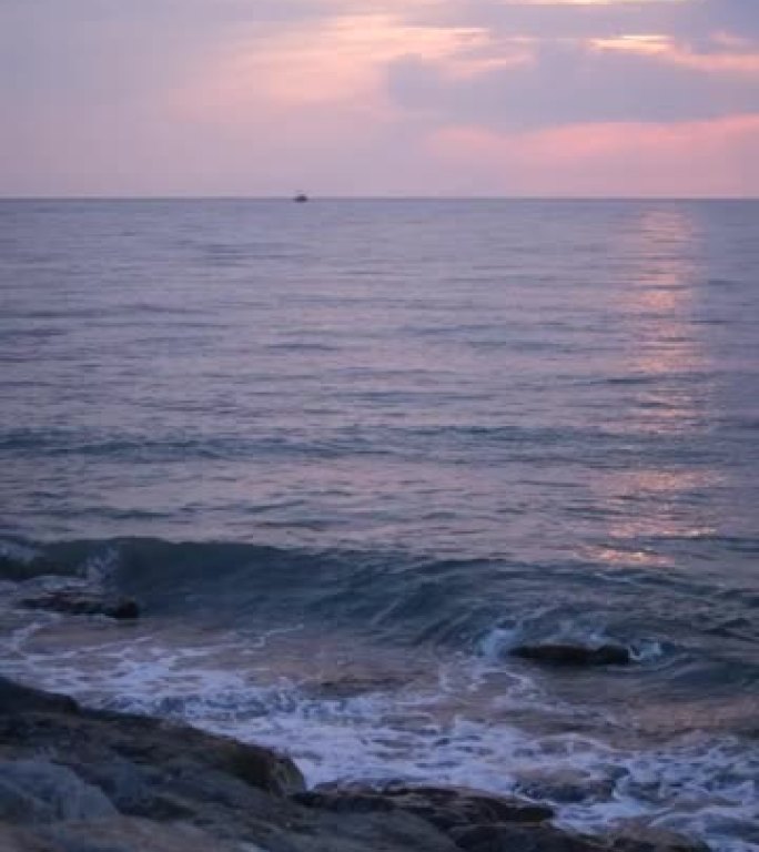 垂直视频。海浪在海上轻拂。有岩石的海岸 .. 鹅卵石很小。日落。地平线。