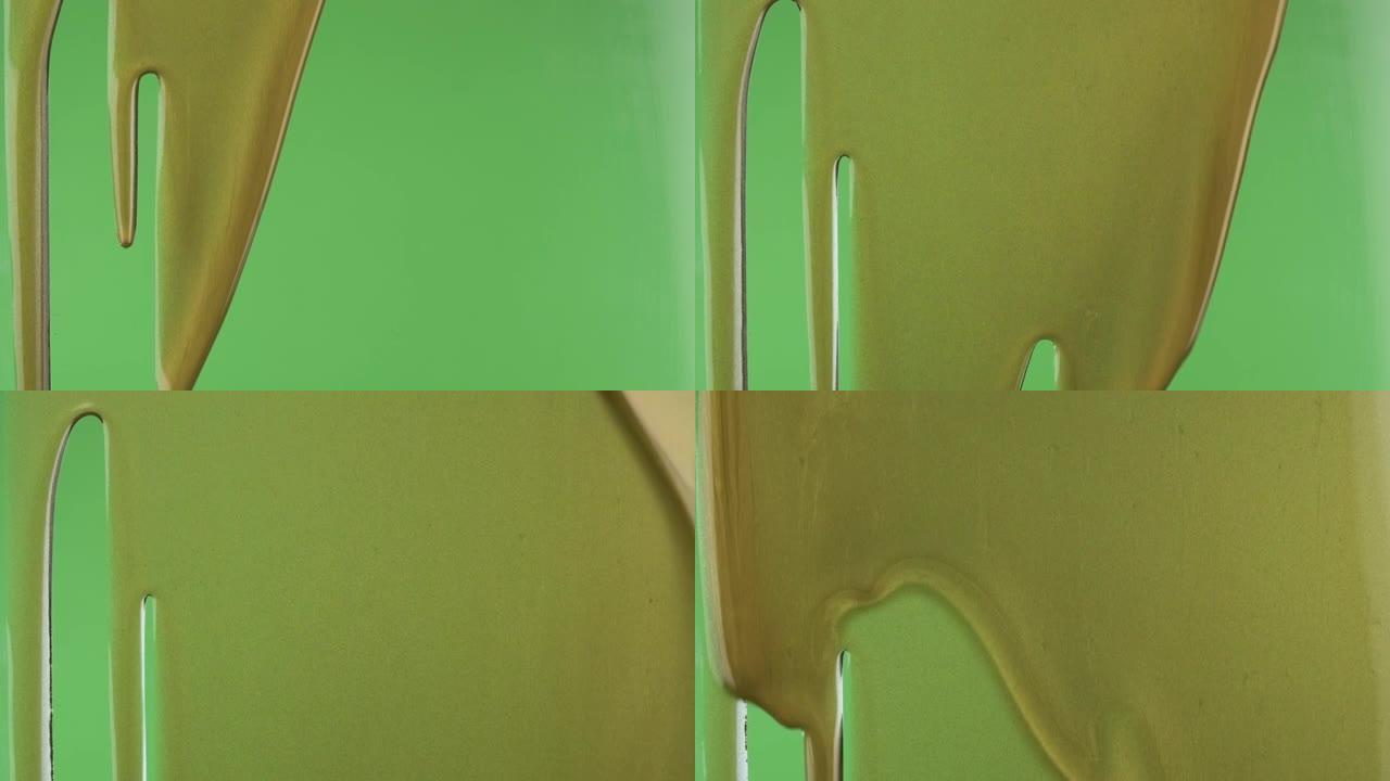 慢动作。绿色背景上的金漆流。金色油漆泄漏的特写