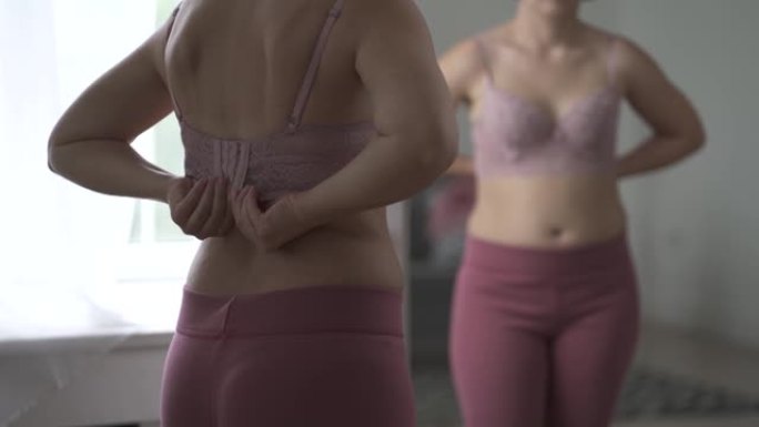 一名妇女在试衣间试穿胸罩，镜子中反射出带有宽扣的紧身胸衣