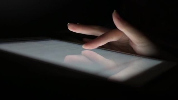 一个女人的手指在平板电脑的屏幕上滑动，可以在不打开灯的情况下播放社交媒体，在睡觉前躺在床上。