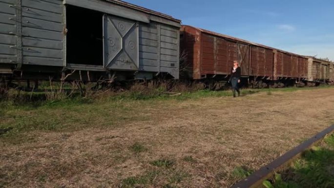 戴着墨镜的成年金发女子走在废弃的货运列车旁边。废弃场所概念