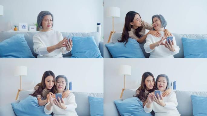 亚洲幸福家庭，老妈在家带女儿用手机。迷人的美丽女孩惊喜年迈的老母亲，坐在沙发上，在家里的客厅网上聊天