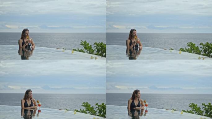 美丽的美国女人在巴厘岛度假胜地的游泳池里喝鸡尾酒