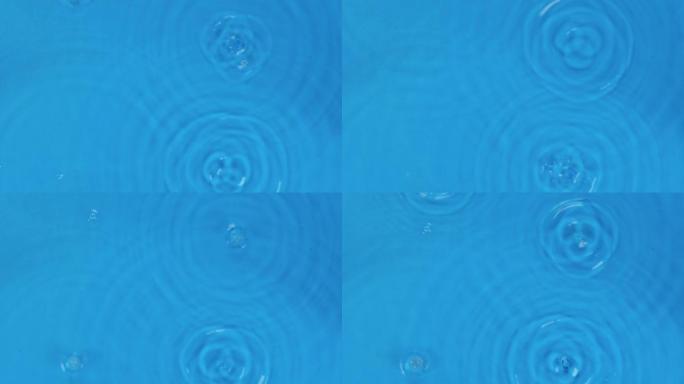 慢动作。四滴落入清澈透明的蓝色水中。圆形透明的水滴，向下落下。飞溅。顶视图。