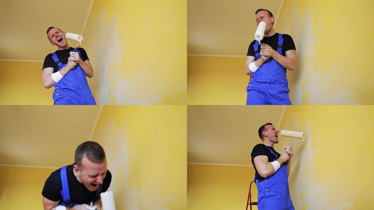 带着油漆滚筒的快乐画家。穿着蓝色工作服的有趣的年轻人工人一边粉刷墙壁一边唱着滚轴。房子里改头换面的快