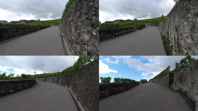 沿着葡萄园之间的乡村小路走，汽车经过。POV街景在美丽的瑞士乡村带鹅卵石墙的老路上坡行走