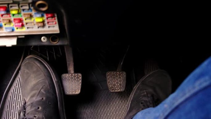 男性的脚在一辆肮脏的旧车里踩踏板。