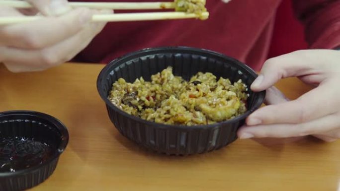 一名男子用塑料板上的一次性木筷子吃亚洲食物。外送或外卖的印度菜: 米饭、咖喱鸡、各种蔬菜