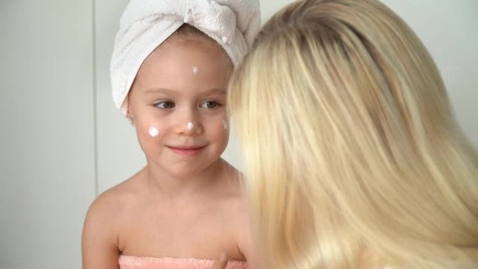 母亲在浴室洗澡后，将乳霜涂在女儿的脸上。婴儿护理