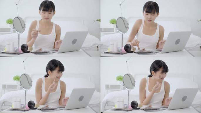 年轻的亚洲女性之美，在笔记本电脑上学习用刷子在脸颊上化妆，在线辅导课程，女性教学，并在流媒体社交媒体