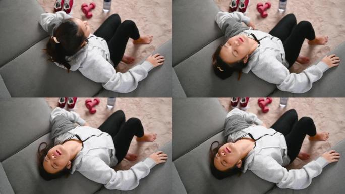 一个穿着运动服的女人在家锻炼后躺在客厅的沙发上筋疲力尽。家庭保健、锻炼和锻炼。健康的生活方式和活动理