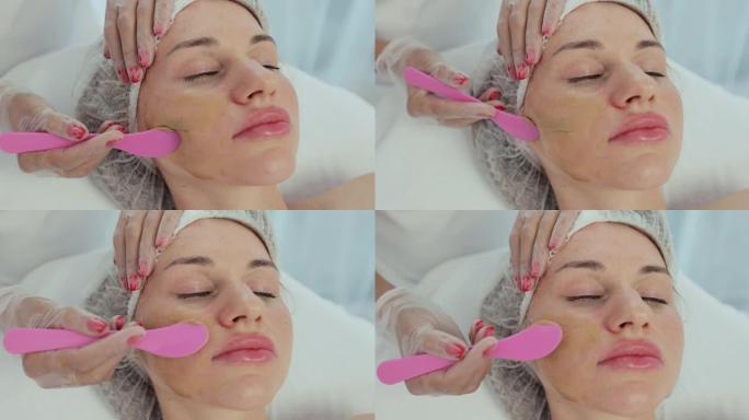 特写美容师用刷子将面膜涂在躺在水疗中心按摩台上的美女脸上。