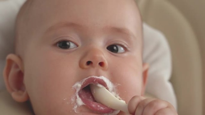 一个满意的孩子拿着勺子，自己吃酸奶。新生儿坐在椅子上独自吃奶酪