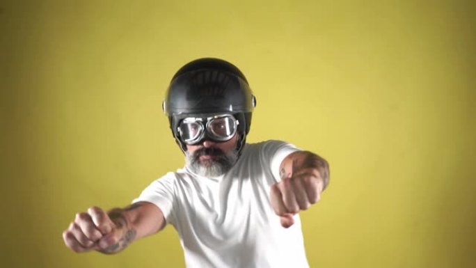 戴着头盔的大胡子男子模拟在黄色背景上驾驶摩托车