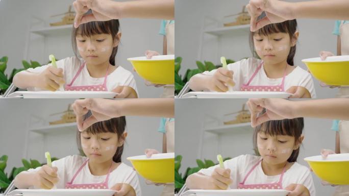 快乐的亚洲孩子在家学习制作饼干，女孩将面粉粉洒到搅拌碗中。慢动作。