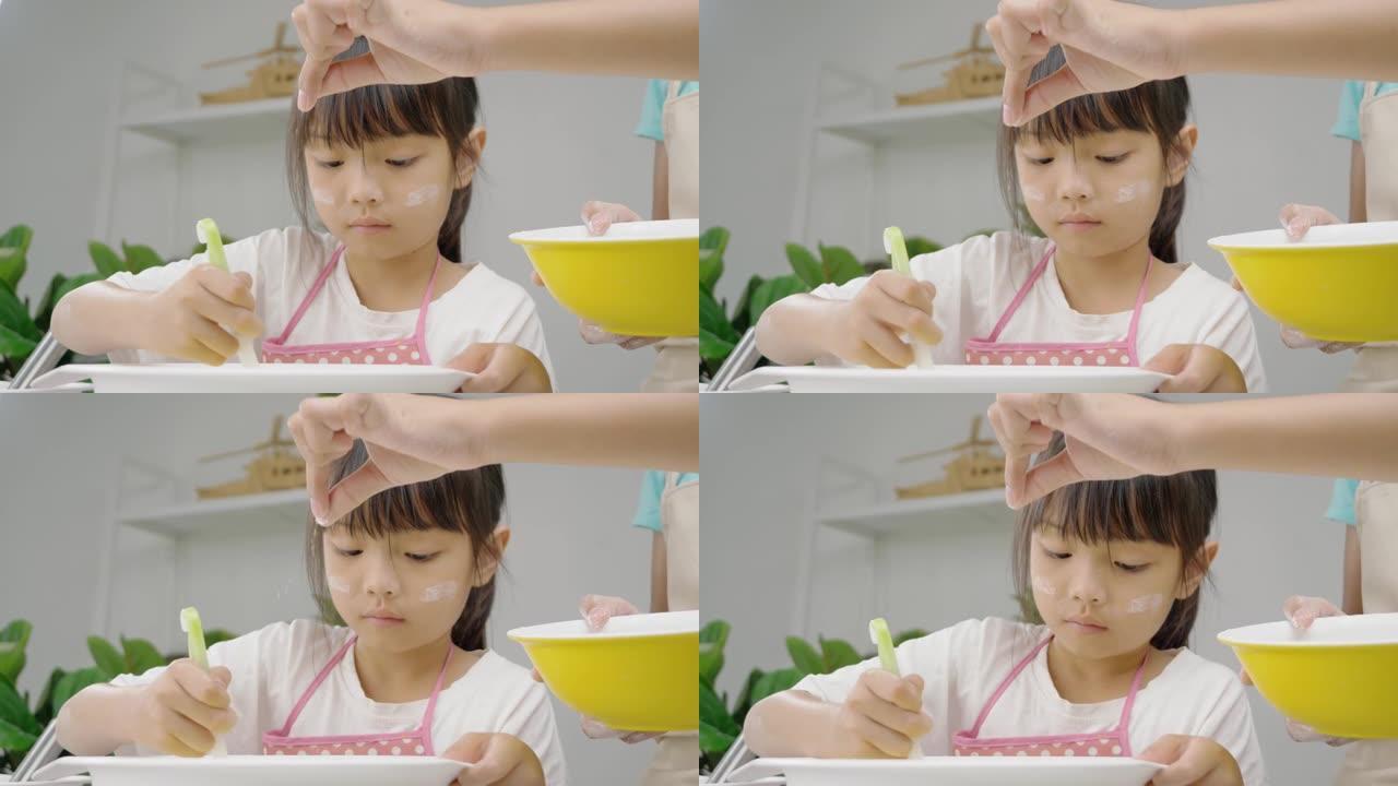 快乐的亚洲孩子在家学习制作饼干，女孩将面粉粉洒到搅拌碗中。慢动作。
