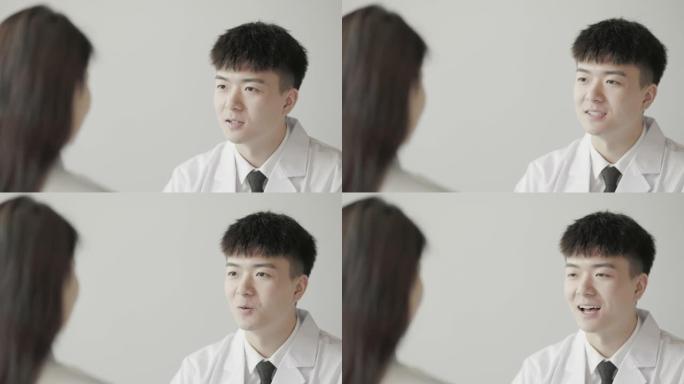 年轻的亚洲男医生正在与坐在他对面的女患者讨论他们的病情。美容医生和整形外科医生在亚洲很受欢迎