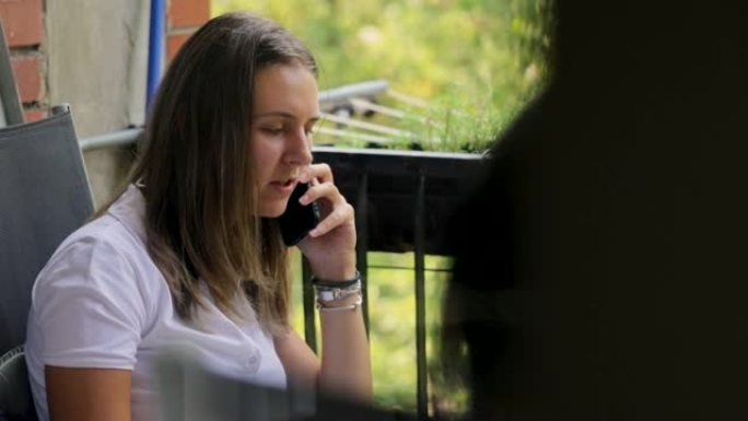 年轻女子在阳台上用手机聊天，同时吸烟和喝咖啡